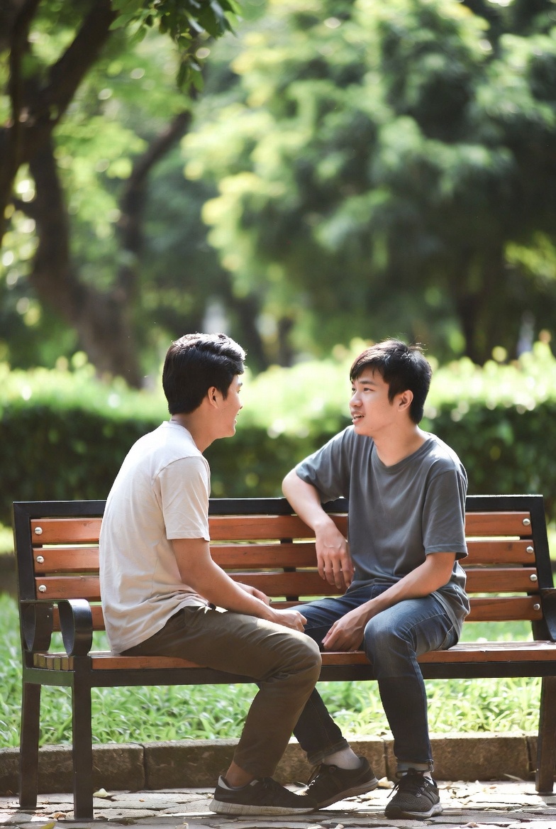 Hai bạn trẻ ngồi đối diện nhau trên ghế công viên trong cuộc trò chuyện chăm chú lắng nghe nhau